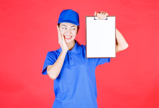 Fille de messagerie en uniforme bleu tenant une liste de tâches et a l'air tenace et confuse.