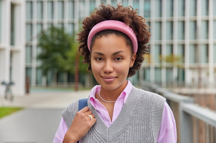 Photo gratuit une fille millénaire assez confiante porte un bandeau de gilet tricoté en chemise rose regarde directement la caméra et marche dehors pendant son temps libre pose à l'extérieur