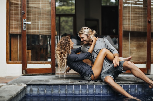 Fille mince embrasse son petit ami bien-aimé et le regarde avec amour. Homme et femme se détendre au bord de la piscine