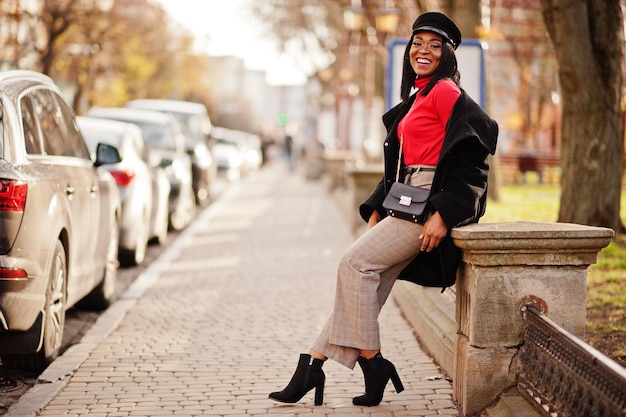 Photo gratuite fille de mode afro-américaine en manteau et casquette de gavroche posée dans la rue