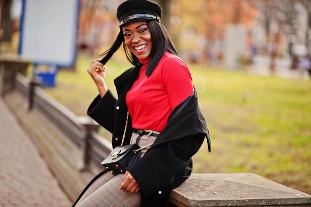 Fille de mode afro-américaine en manteau et casquette de gavroche posée dans la rue