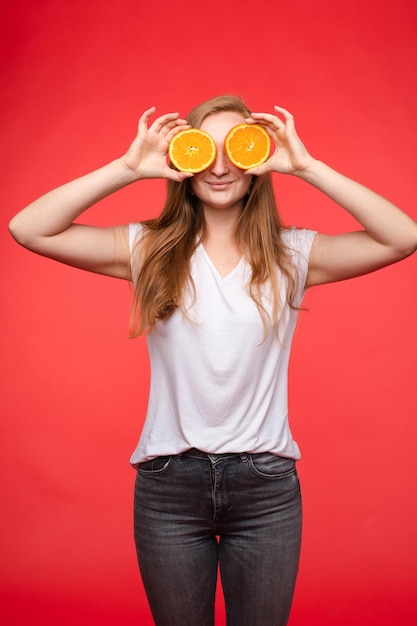 Fille à la mode drôle avec coiffure tenant des oranges sur les yeux.