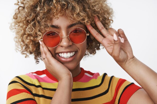 fille montrant un geste de paix et touchant la joue timide et mignonne exprimant une attitude positive et de la tendresse s'amusant sur le blanc.