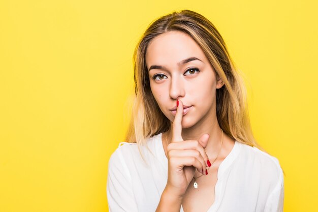 Fille montrant signe de silence isolé sur mur jaune