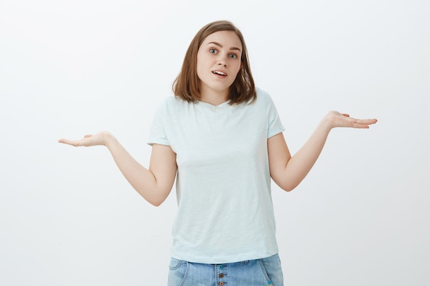 La fille n'a aucune idée. Portrait de jolie jeune étudiante désemparée aux cheveux bruns en t-shirt à la mode en haussant les épaules avec les paumes écartées et l'expression confuse ignorant ce qui s'est passé