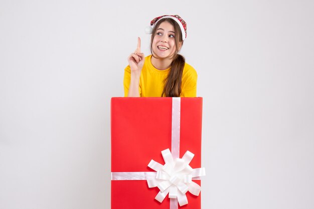 Fille de Noël heureux avec bonnet de Noel debout derrière un grand cadeau de Noël sur blanc