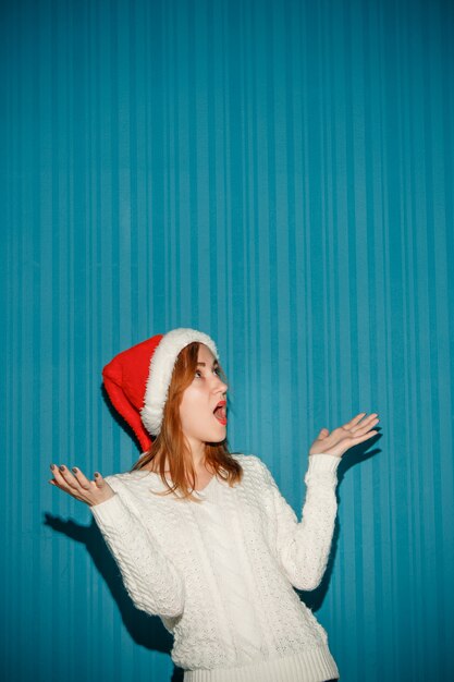 fille de Noël surpris portant un bonnet de Noel sur le fond bleu studio