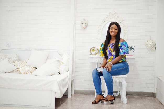 Fille noire afro-américaine du millénaire dans le salon avec téléphone portable aux mains heureuse jeune femme à la peau sombre le week-end à la maison