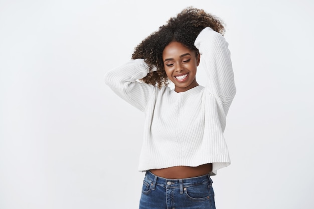 Fille à la peau foncée féminine tendre et insouciante posant sur un mur blanc