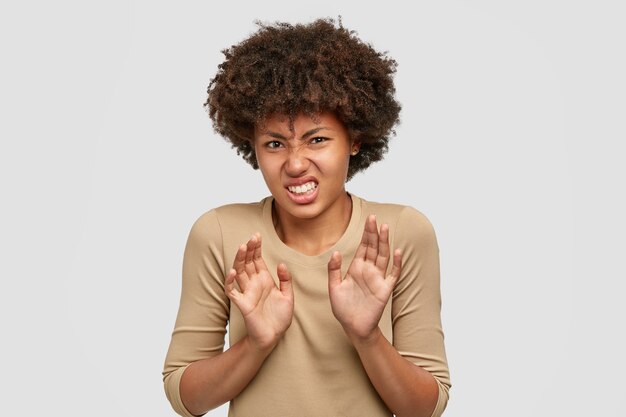 Une fille à la peau sombre et insatisfaite intense, fronce les sourcils de mécontentement, ressent de l'aversion, tire les mains en signe de refus