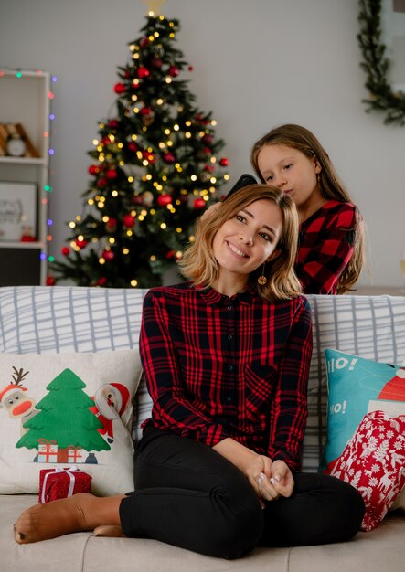 Fille peignant ses cheveux de mère souriante assis sur un canapé et profiter du temps de Noël à la maison