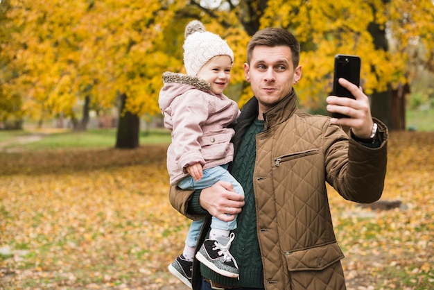 Fille père et enfant en bas âge faisant selfie dans le parc en automne