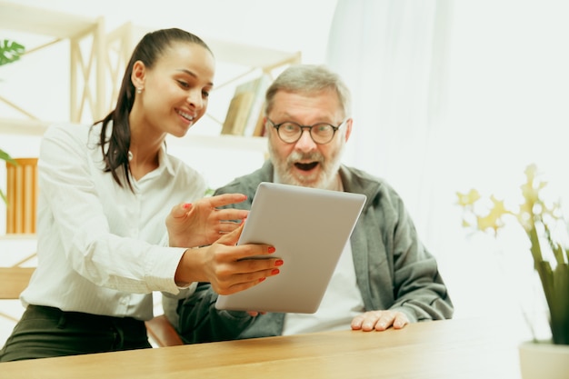 Une fille ou une petite-fille passe du temps avec le grand-père ou l'homme âgé. Fête de la famille ou des pères, émotions et bonheur. Portrait de mode de vie à la maison. Fille prenant soin de papa. Utilisation d'une tablette.