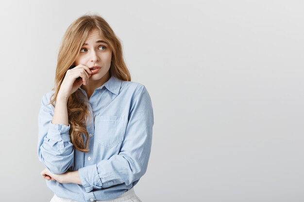 La fille a peur que quelqu'un connaisse le secret. Tir intérieur d'une femme européenne timide en insécurité en chemisier bleu, mordre les ongles et à côté avec expression nerveuse, être anxieux en attente d'examen