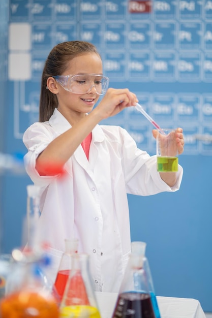 Fille avec pipette sur tube à essai debout dans la salle de classe