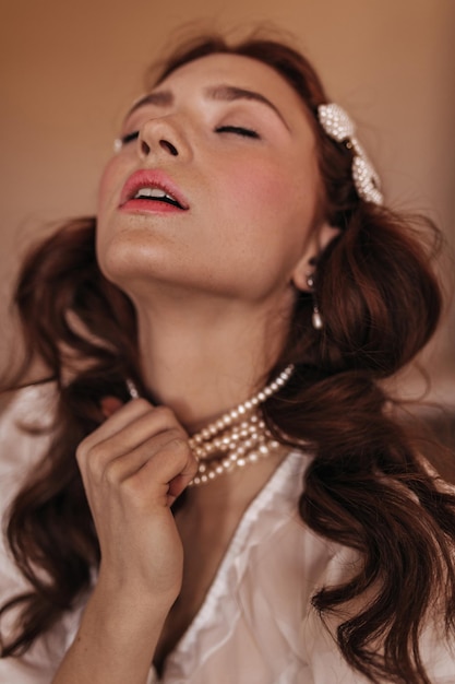 Fille avec plaisir essaie d'enlever son collier de perles Portrait de femme en tenue blanche