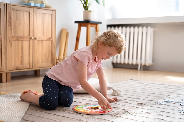 Fille en plein plan jouant sur le sol avec un puzzle