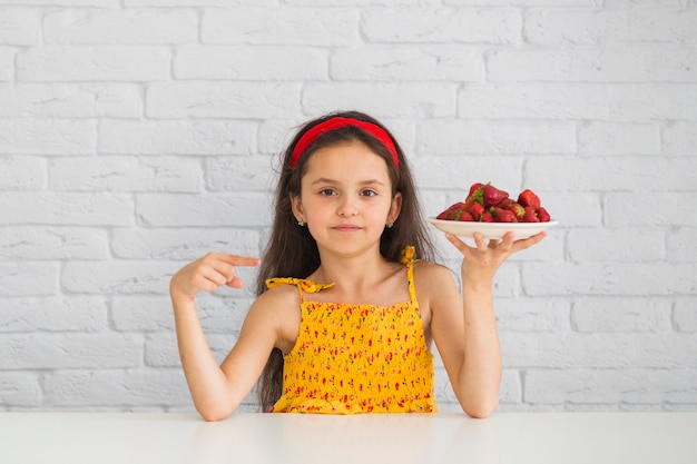 Fille pointant sur une assiette avec de la fraise fraîche