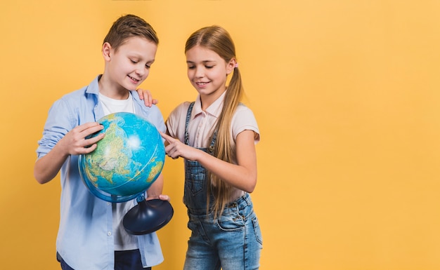 Fille pointant sur le globe, tenue par son ami sur fond jaune