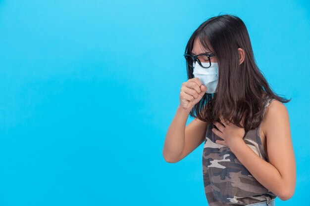 Une fille portant un masque montrant la toux éternue sur un mur bleu