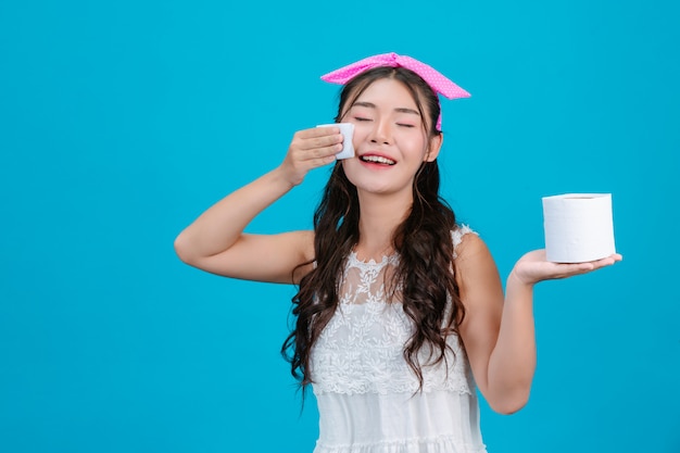 Fille portant un pyjama blanc, utilisant du papier de soie sur son visage sur un fond bleu.