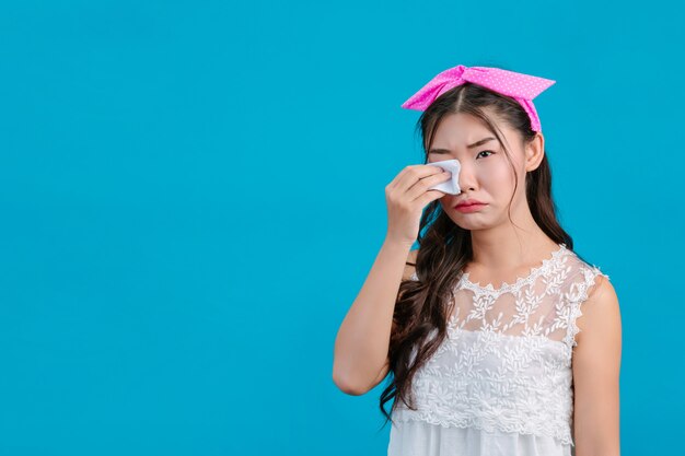 Fille portant un pyjama blanc, utilisant du papier de soie sur son visage sur un fond bleu.