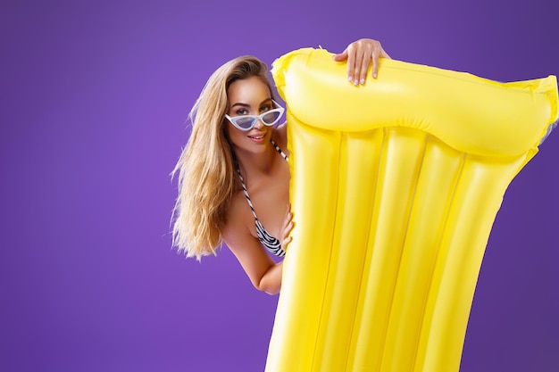 Fille positive en bikini va voter avec fond de studio violet matelas gonflable jaune