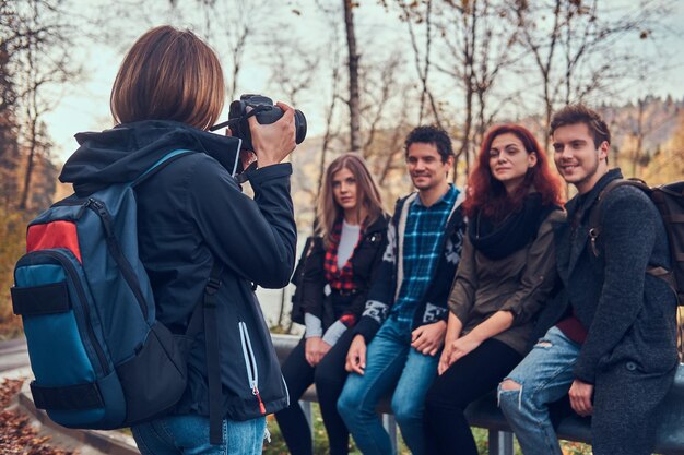 Fille prenant une photo de ses amis. Groupe de jeunes amis assis sur un garde-corps près de la route. Voyage, randonnée, concept d'aventure.