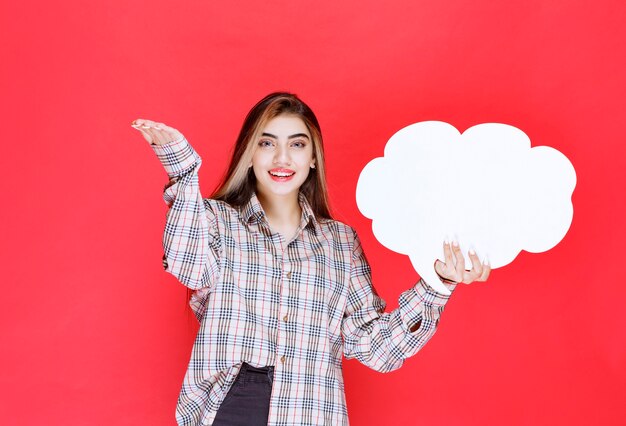 Fille en pull chaud tenant un tableau d'idées en forme de nuage et nommant la personne devant