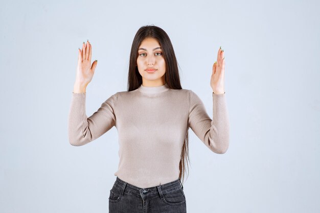 Fille en pull gris montrant les dimensions d'un objet.