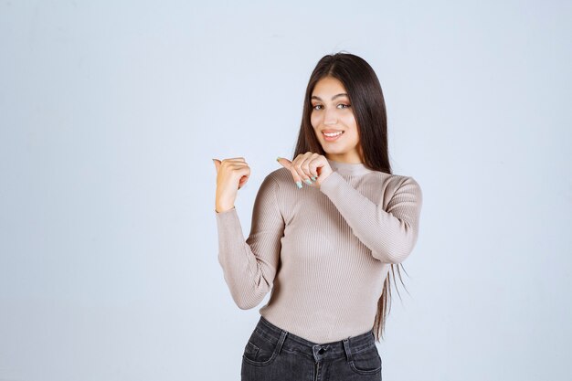 Fille en pull gris montrant quelque chose sur la gauche.