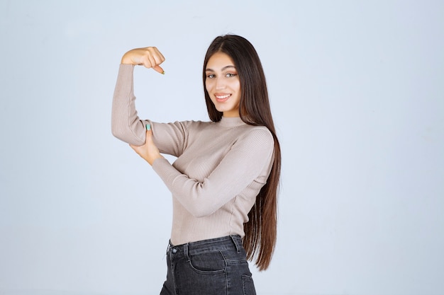 Fille en pull gris montrant ses poings et sa puissance.