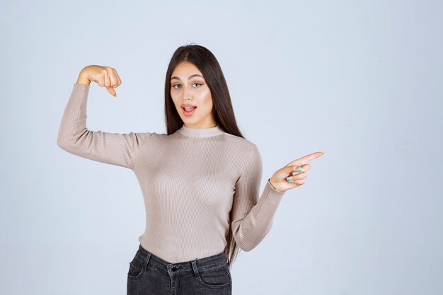 Fille en pull gris montrant ses poings et sa puissance.