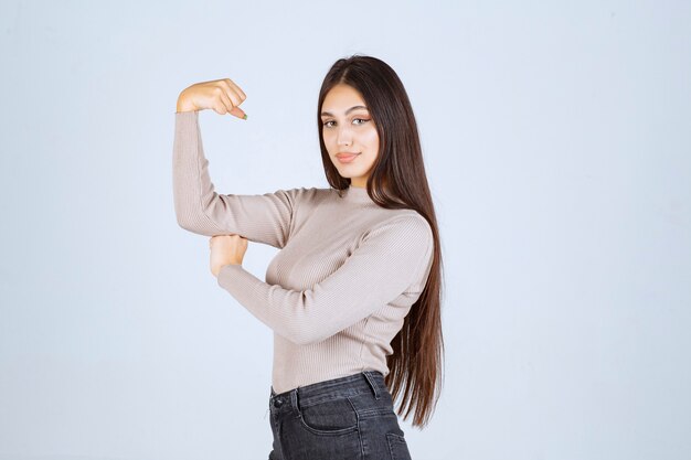 Fille en pull gris montrant ses poings et sa puissance.