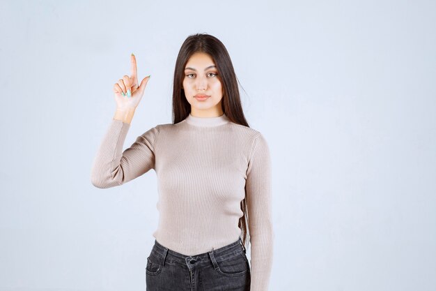 Fille en pull gris pointant quelque chose au-dessus.