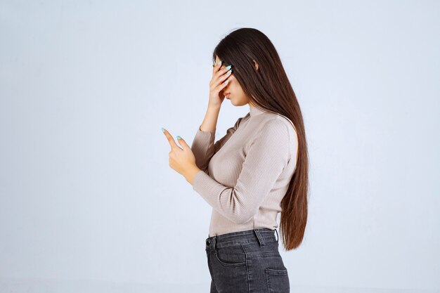 Fille en pull gris tenant son visage et sa tête.