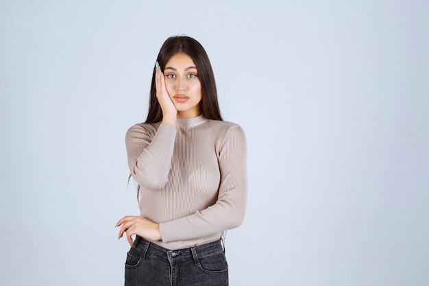 Fille en pull gris tenant son visage et sa tête.