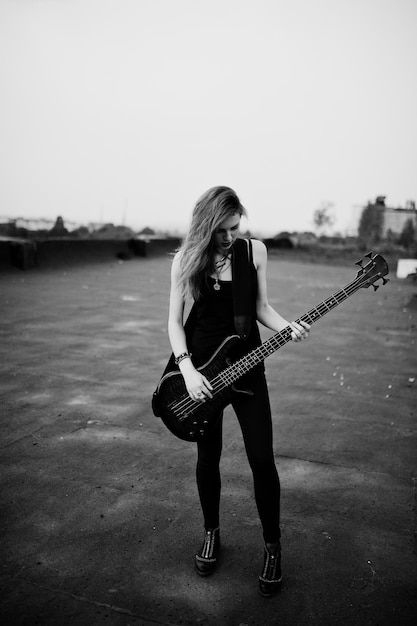 Photo gratuite fille punk aux cheveux rouges portant du noir avec une guitare basse sur le toit