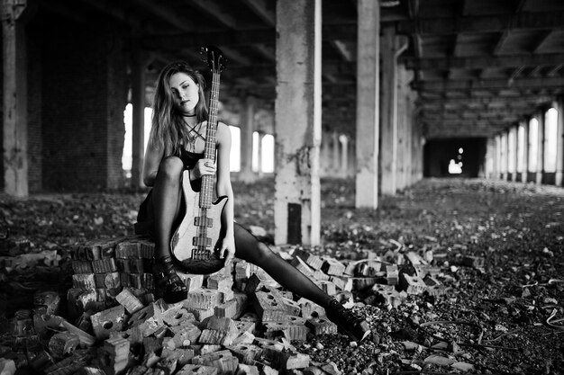 Fille punk aux cheveux rouges portant une jupe noire et rouge avec une guitare basse à un endroit abandonné Portrait d'une musicienne gothique