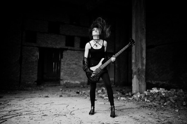 Fille punk aux cheveux rouges portant sur noir avec guitare basse à l'endroit abandonné Portrait d'une musicienne gothique