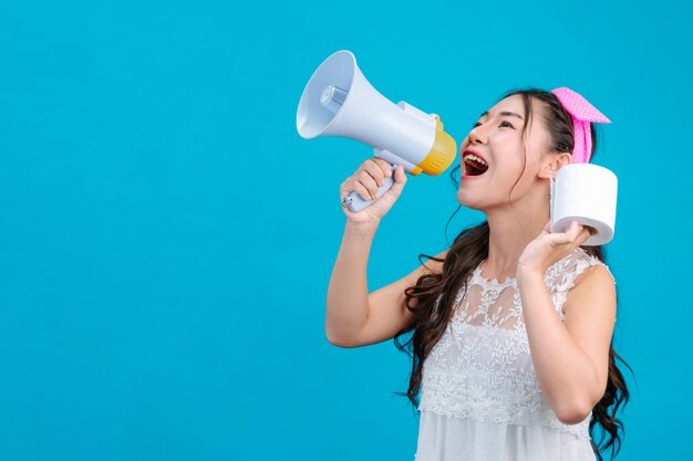 : Une fille en pyjama blanc tenant un mégaphone et tenant un papier de soie à la main sur un bleu.