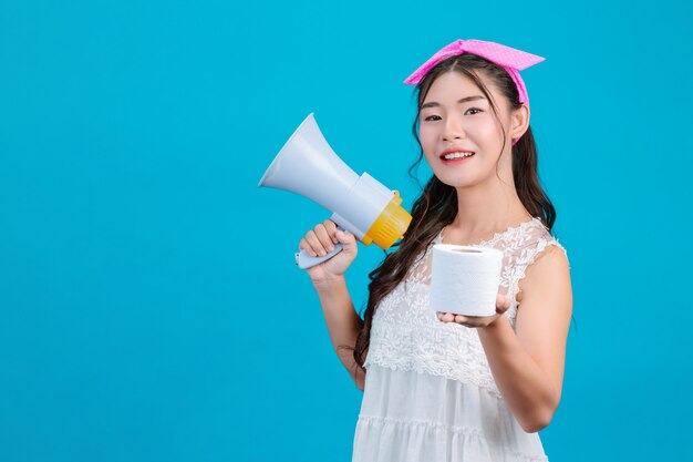 : Une fille en pyjama blanc tenant un mégaphone et tenant un papier de soie à la main sur un bleu.