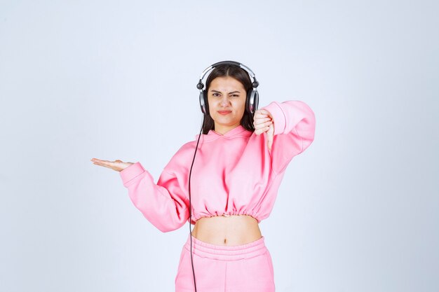 Fille en pyjama rose écoutant des écouteurs et n'aime pas la musique. Photo de haute qualité