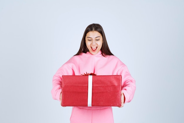 Fille en pyjama rose serrant une grande boîte-cadeau rouge et souriant.
