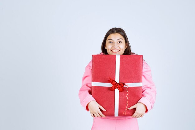 Fille en pyjama rose serrant une grande boîte-cadeau rouge et souriant.