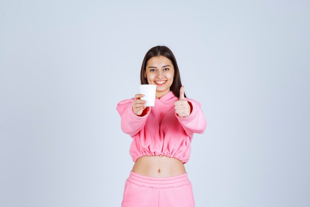 Fille en pyjama rose tenant une tasse de café et appréciant le goût