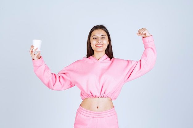 Fille en pyjama rose tenant une tasse de café et montrant son poing