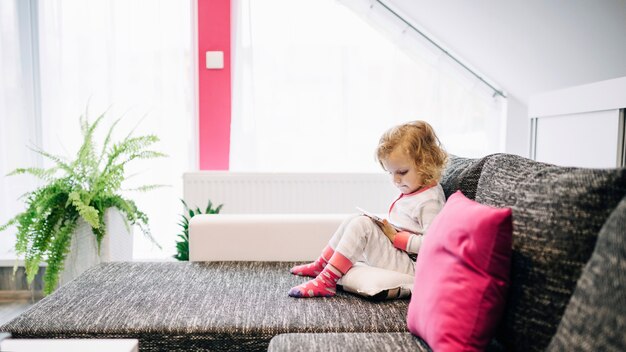 Fille en pyjama avec tablette sur canapé