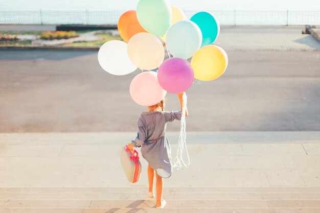 Fille qui court dans les escaliers tenant des ballons colorés et une valise enfantine