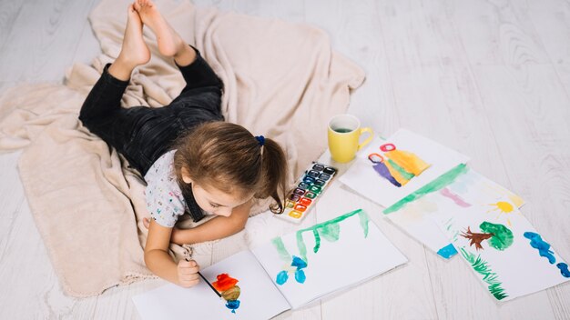 Fille qui peint à l&#39;aquarelle sur du papier près de dessine et se trouvant sur le sol